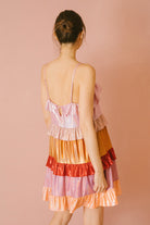 Back view of a woman wearing a colorful iridescent tiered dress against a pink background