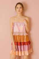Woman wearing a colorful iridescent tiered dress against a pink background