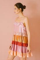 Side view of a woman wearing a colorful iridescent tiered dress against a pink background