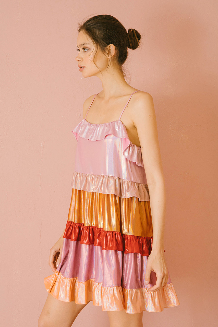 Side view of a woman wearing a colorful iridescent tiered dress against a pink background