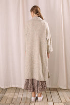 Back view of a woman in a long grey cardigan standing against a brick wall