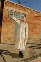 Woman in a long grey cardigan standing against a brick wall.