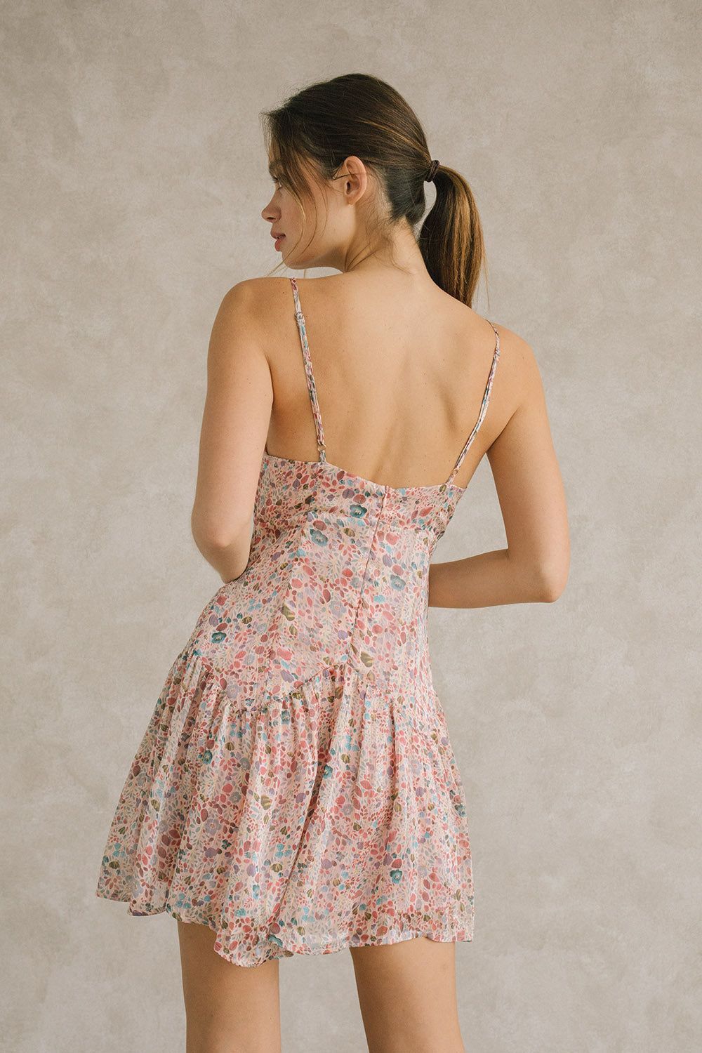 A woman viewed from behind wearing a floral mini dress that features an invisible zipper and adjustable straps.