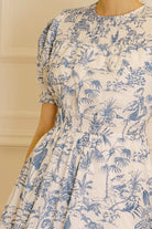 A blue and white tropical print dress against a beige wall.