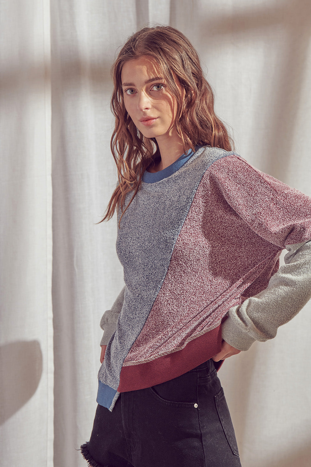 Side view of a woman wearing a color block sweatshirt with round neckline with a plain background