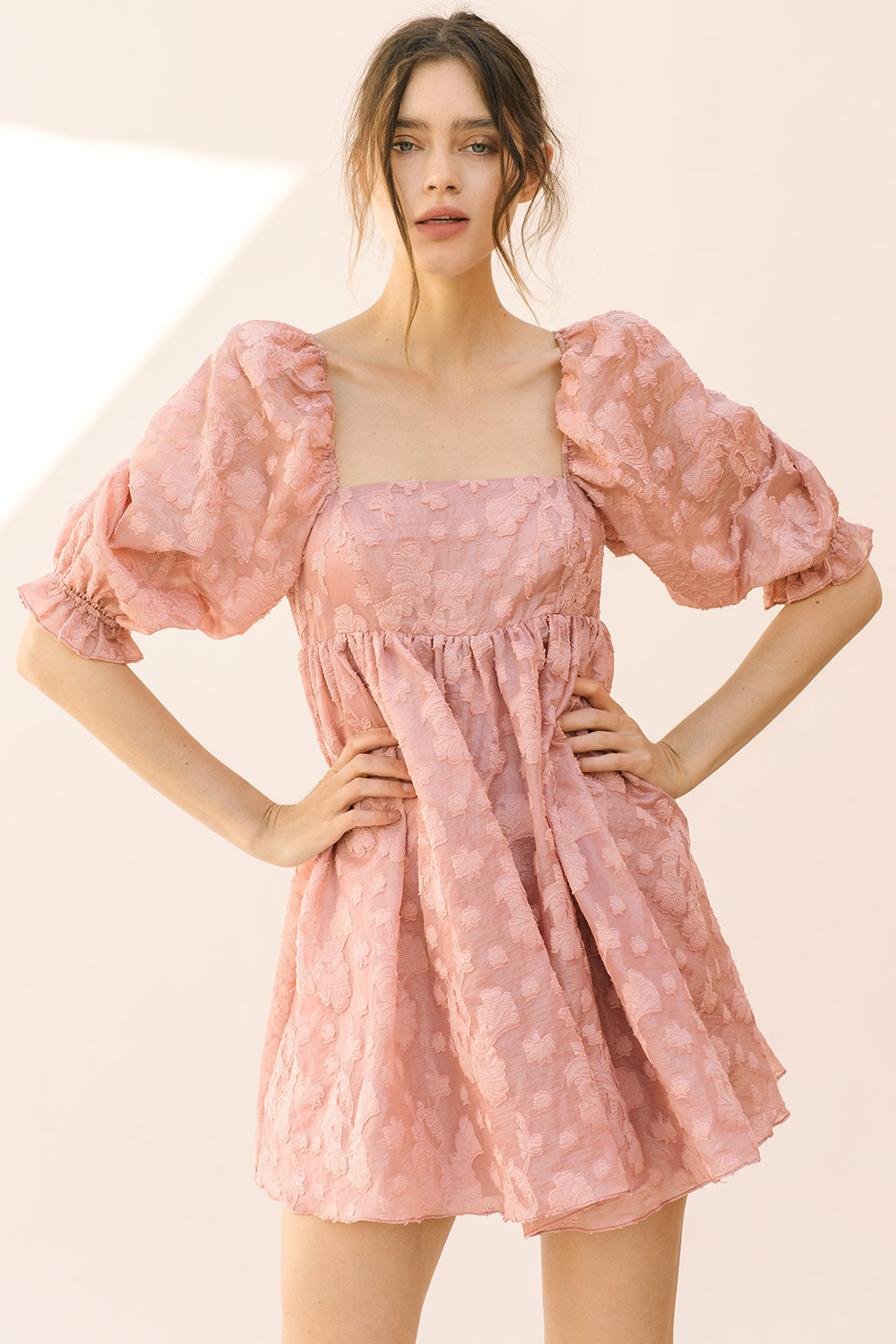 Woman wearing a dark pink mini dress with puff sleeves against a beige background