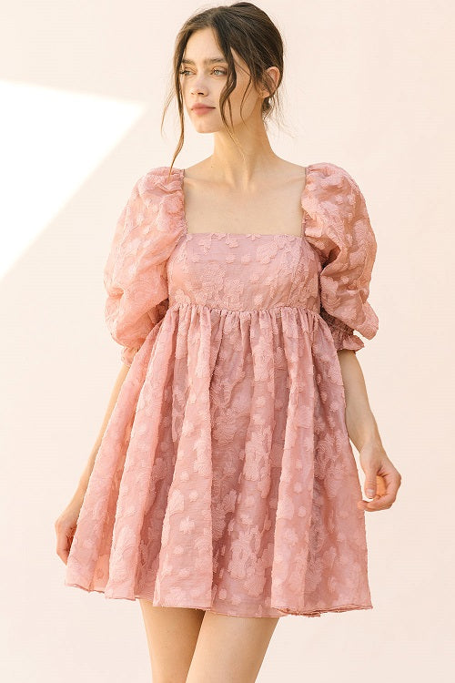 Woman wearing a pink dress with puff sleeves against a beige background