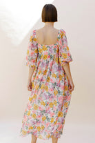 Back view of a woman wearing a pink floral midi dress against a plain background