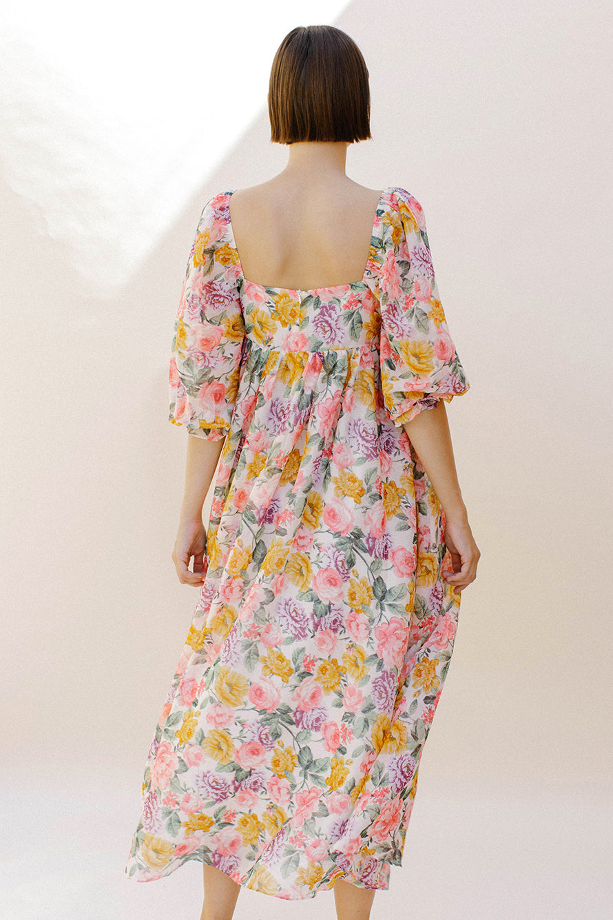 Back view of a woman wearing a pink floral midi dress against a plain background