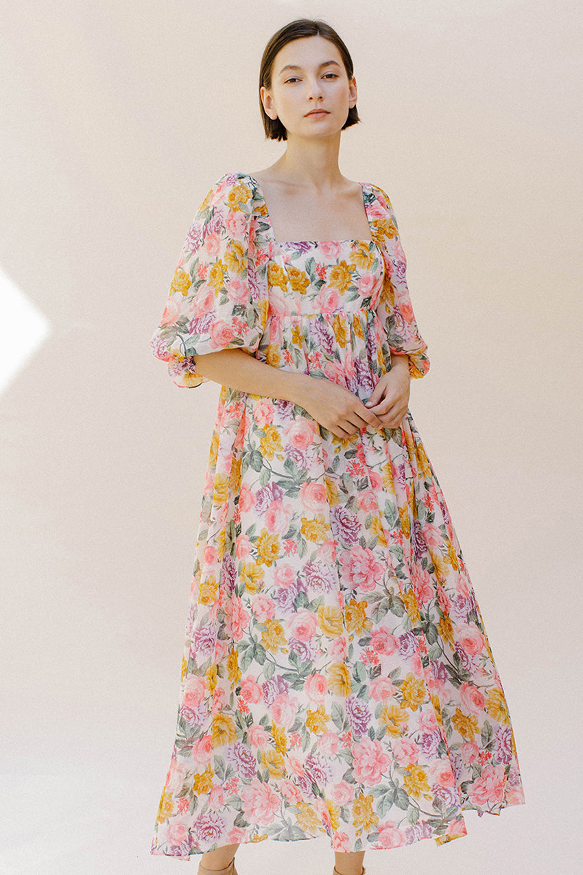 Woman wearing a pink floral midi dress against a plain background