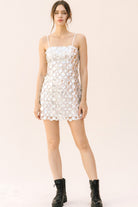 Woman wearing a sequin mini dress and black boots on a beige background