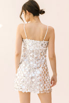 Back view of a woman wearing a sequin mini dress on a beige background