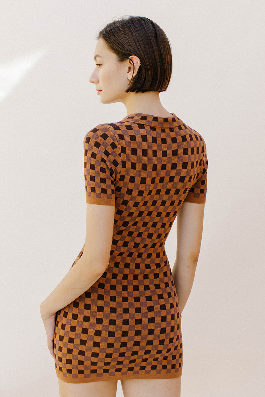 Back view of a woman wearing a brown and dark brown checkered dress against a plain background