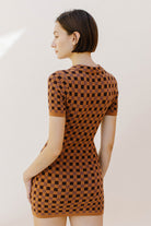Back view of a woman wearing a brown and dark brown checkered dress against a plain background