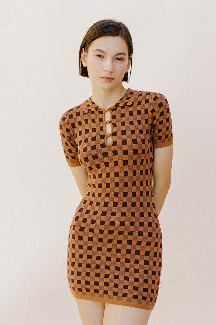 Woman wearing a brown and dark brown checkered dress against a plain background