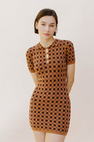 Woman wearing a brown and dark brown checkered dress against a plain background