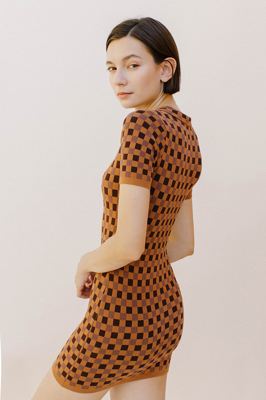 Side view of a woman wearing a brown and dark brown checkered dress against a plain background