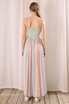 Back view of a woman wearing a pastel striped dress standing against a plain background