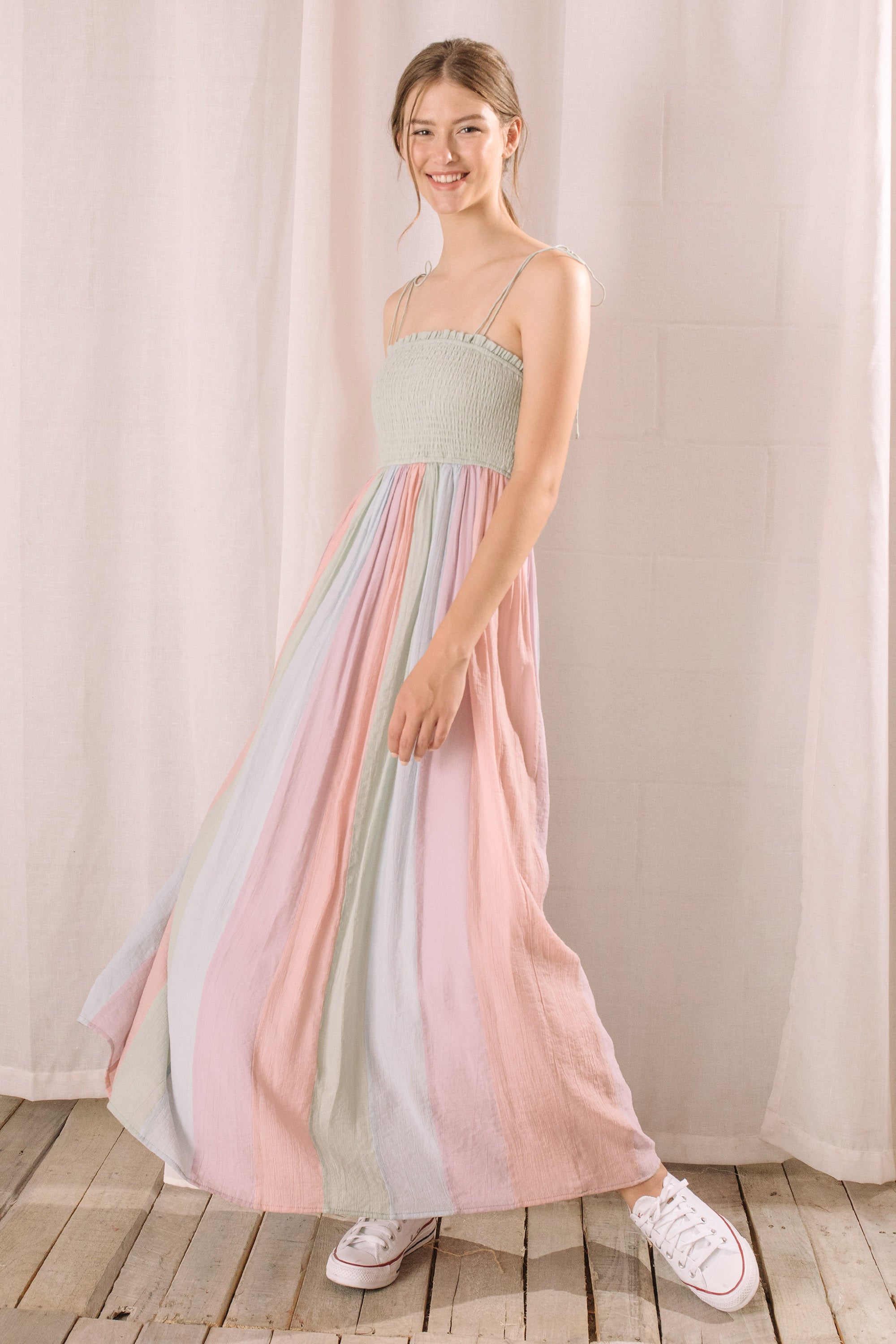 Side view of a woman wearing a pastel striped dress standing against a plain background