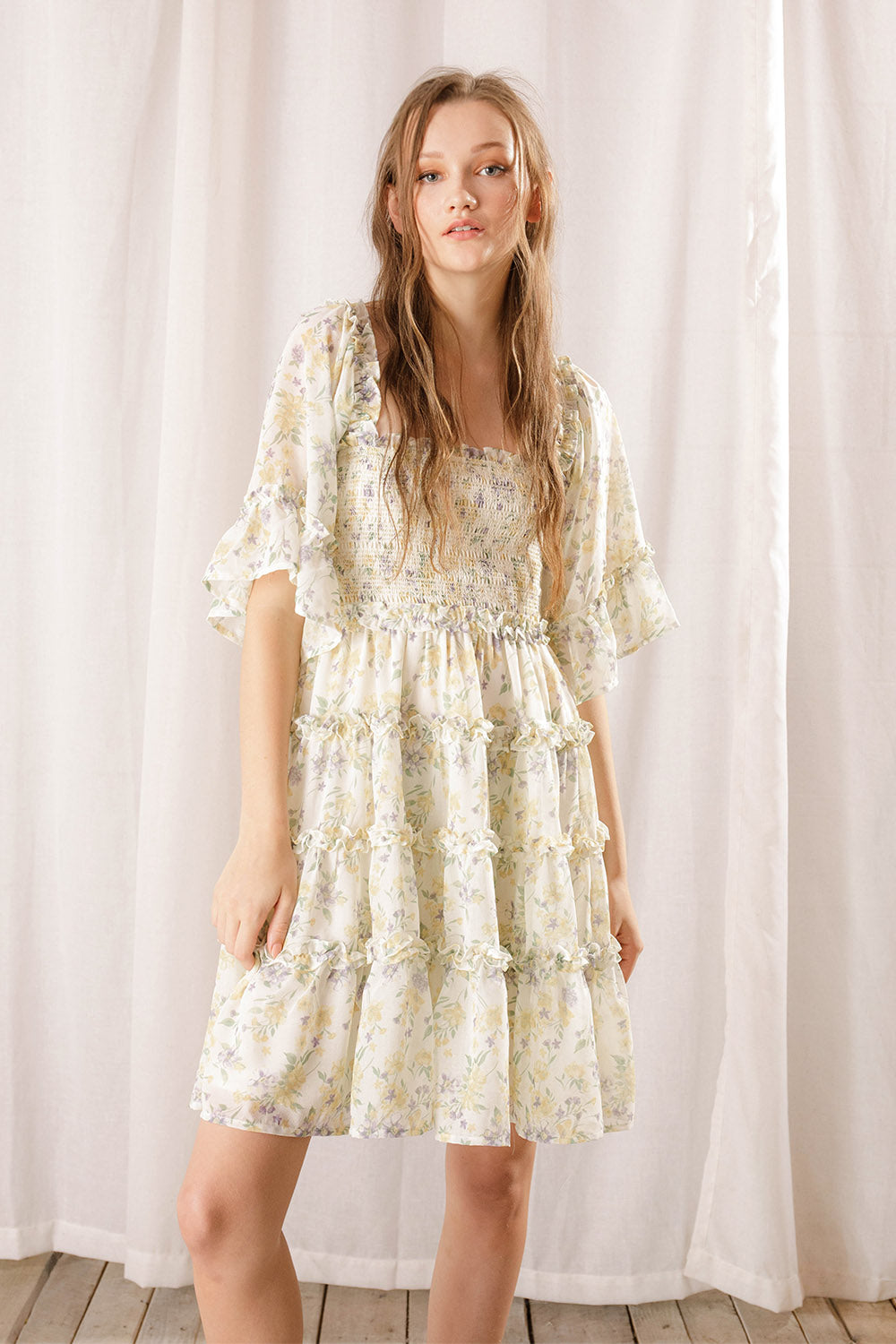 Woman wearing an ivory floral dress against a white curtain background