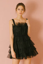 Woman wearing a black tulle tiered dress against a pink background