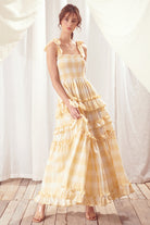 Woman wearing a yellow checkered dress standing against a white curtain.