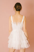 Back of a woman wearing a white tiered dress against a pink background