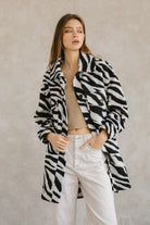 Woman wearing a zebra-patterned coat and white jeans against a plain background