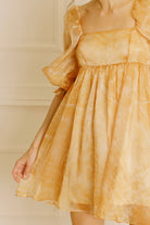A yellow dress with puff sleeves against a neutral wall.