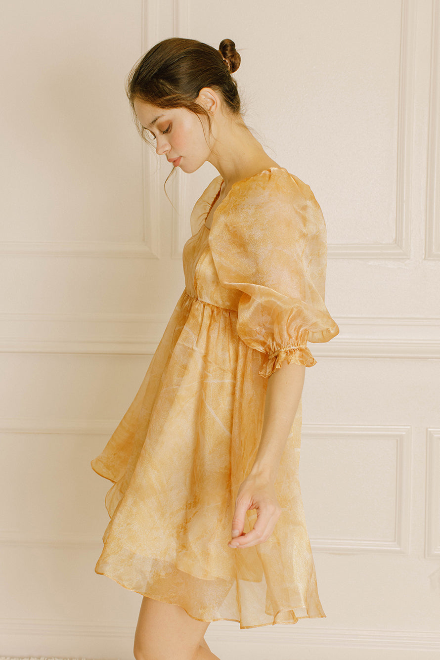 Side view of a woman wearing a yellow dress with puff sleeves against a neutral wall.